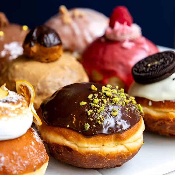 Assortment of gourmet donuts with various toppings like chocolate, pistachio, raspberry, and Oreo.