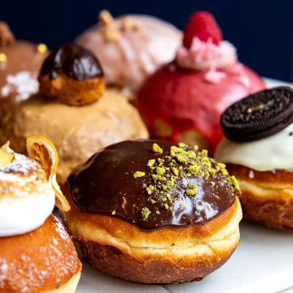 Assortment of colorful, frosted donuts with various toppings, including chocolate, pistachio, and fruit.