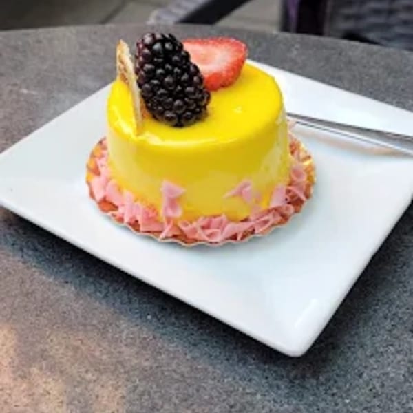 A vibrant yellow mini cake with a glossy glaze, topped with a blackberry and strawberry slice.