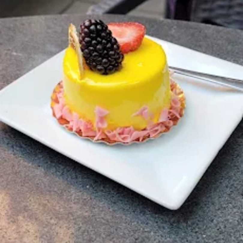A vibrant yellow mini cake with a glossy glaze, topped with a blackberry and strawberry slice.