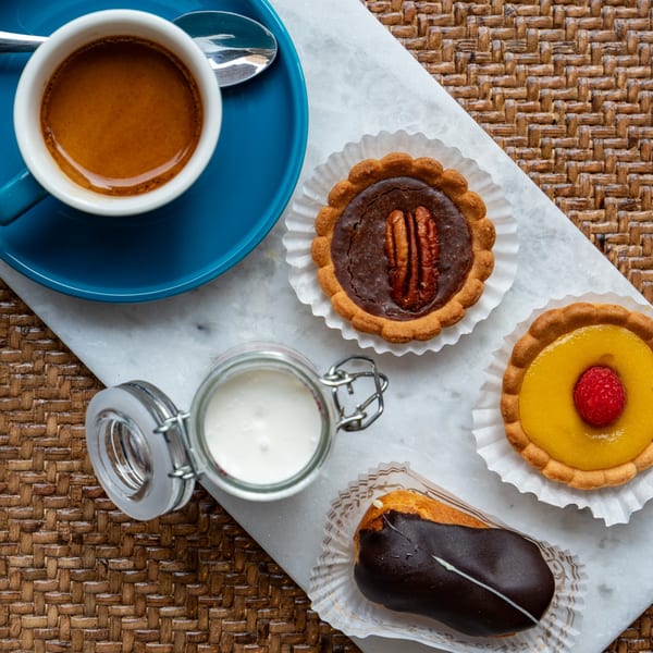 Overhead view of espresso, milk, a chocolate pecan tart, a lemon raspberry tart, and a chocolate eclair.