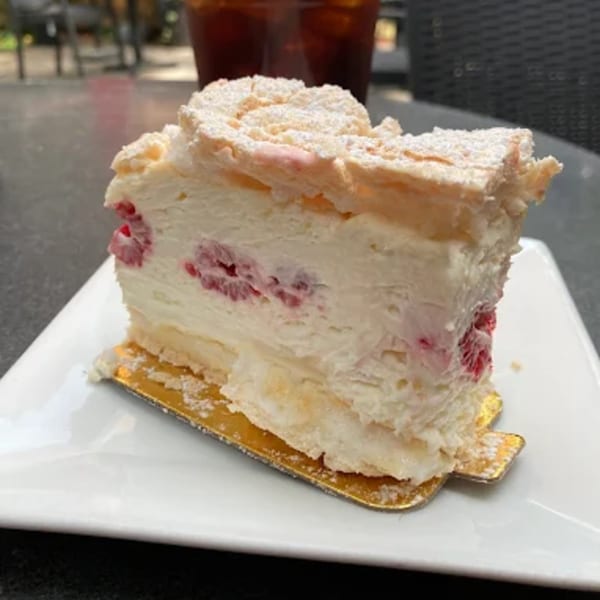 A slice of raspberry meringue cake with powdered sugar on a white plate.