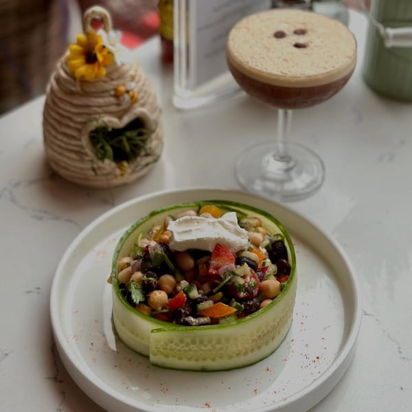 A cucumber-wrapped salad with chickpeas, vegetables, and a dollop of cream, next to an espresso martini.