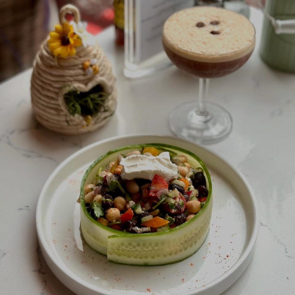A cucumber-wrapped salad with chickpeas, vegetables, and a dollop of cream, next to an espresso martini.