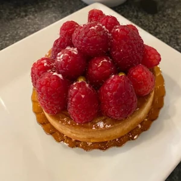 A raspberry tart with powdered sugar on a white square plate.