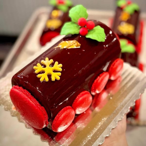A festive chocolate Yule log cake with red macarons, a yellow snowflake, and holly decorations.