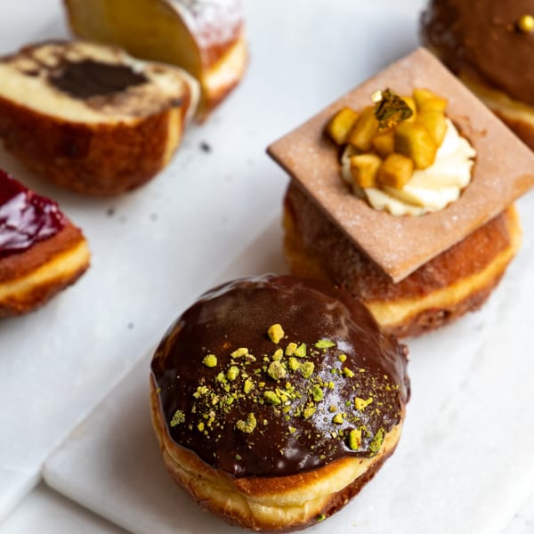 Assortment of gourmet donuts, including chocolate pistachio, jam-filled, and a square pastry-topped donut.