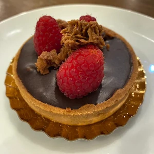 Chocolate tart with fresh raspberries and a crumble topping on a white plate.